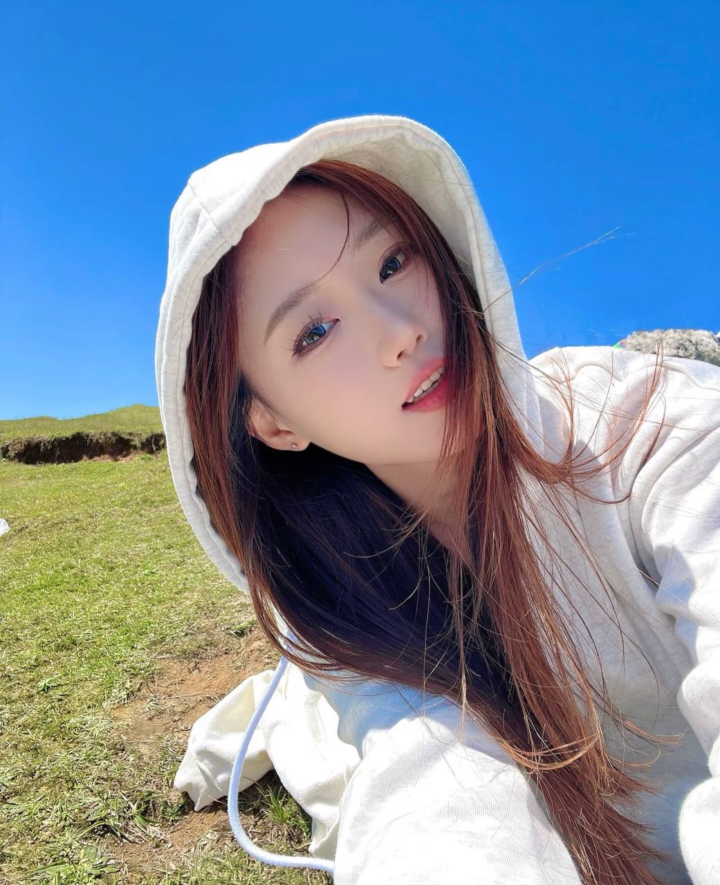 Close-up portrait in a white hoodie, with blue skies and a grassy field