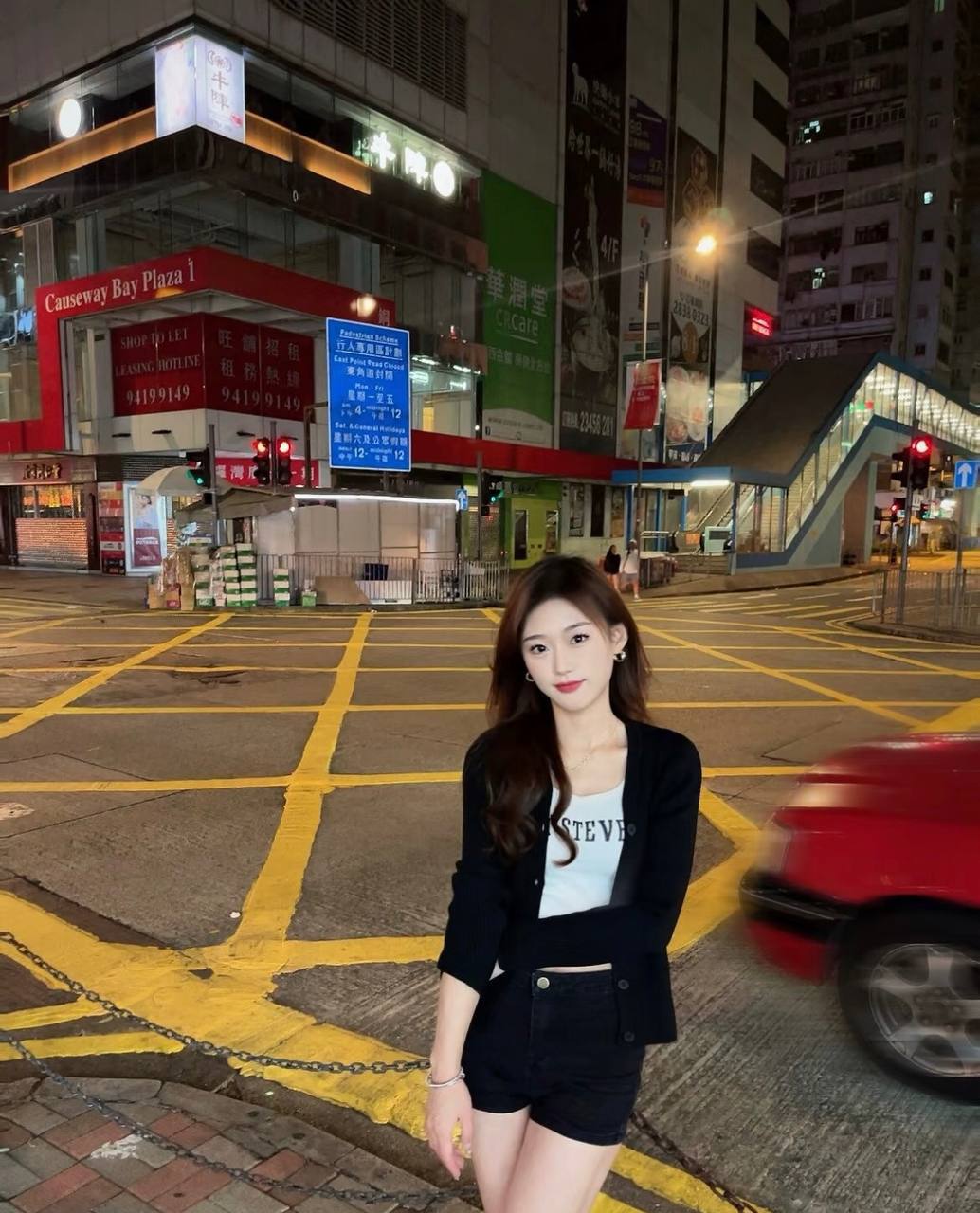 Nighttime street photo beside yellow junction markings, with a red vehicle passing by