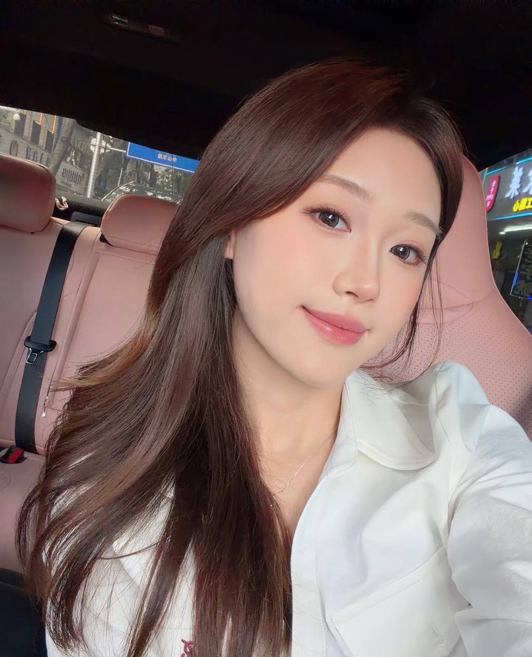 Smiling selfie in a white shirt, with a pink car seat in the background