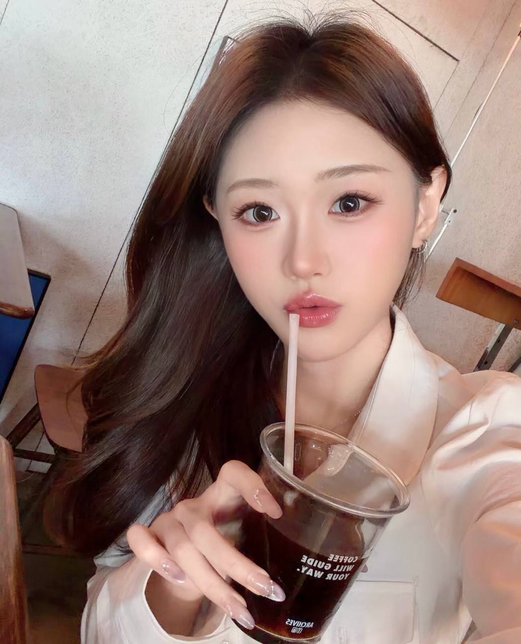Close-up cafe selfie holding an iced drink and sipping through a straw