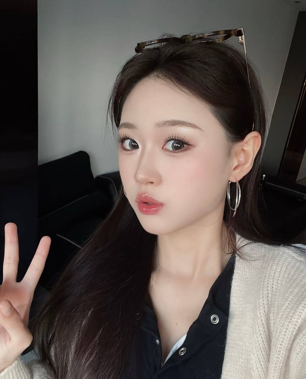Selfie in a light cardigan and black top, wearing large earrings and making a peace sign