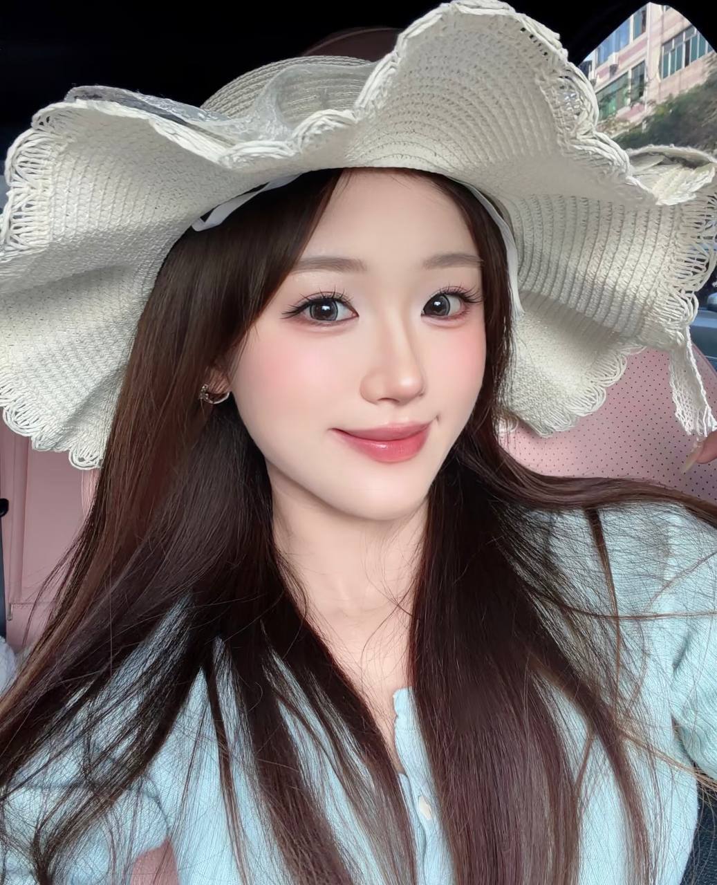 Smiling selfie in a car, wearing a wide-brimmed white straw hat and a light blue top