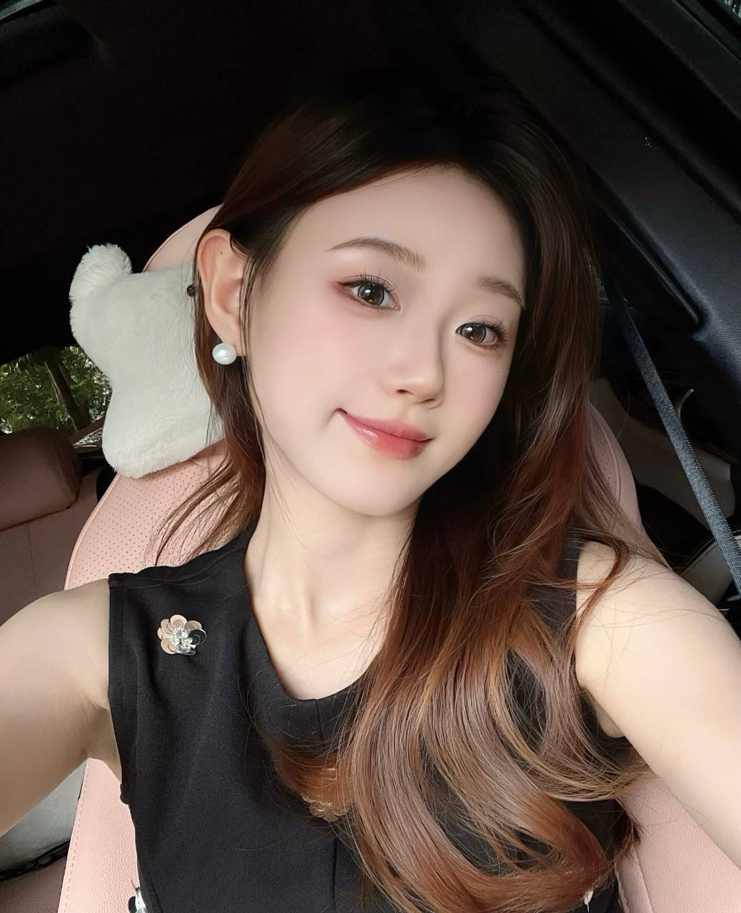 Smiling portrait in a car, wearing a black sleeveless top and pearl earrings