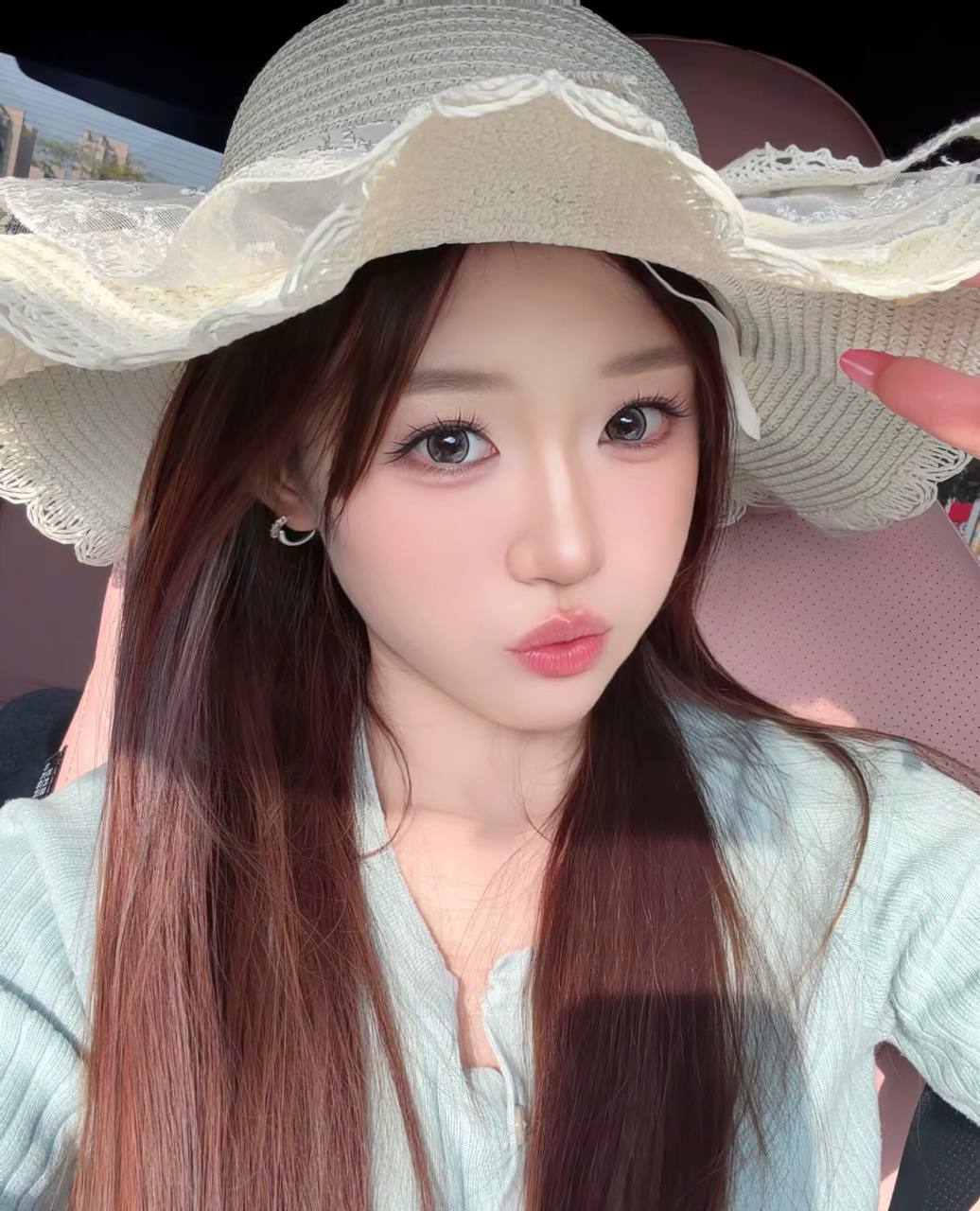 Close-up selfie in a car, wearing a wide-brimmed white straw hat and a light blue top